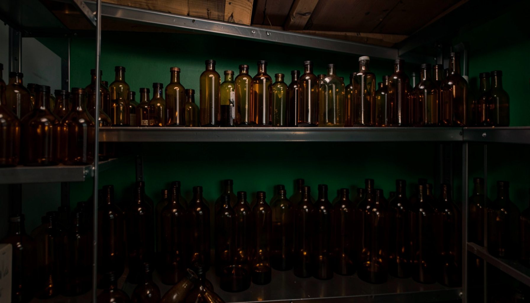Amber glass bottles on metal shelving in a dimly lit storage room, warm brown and charcoal tones